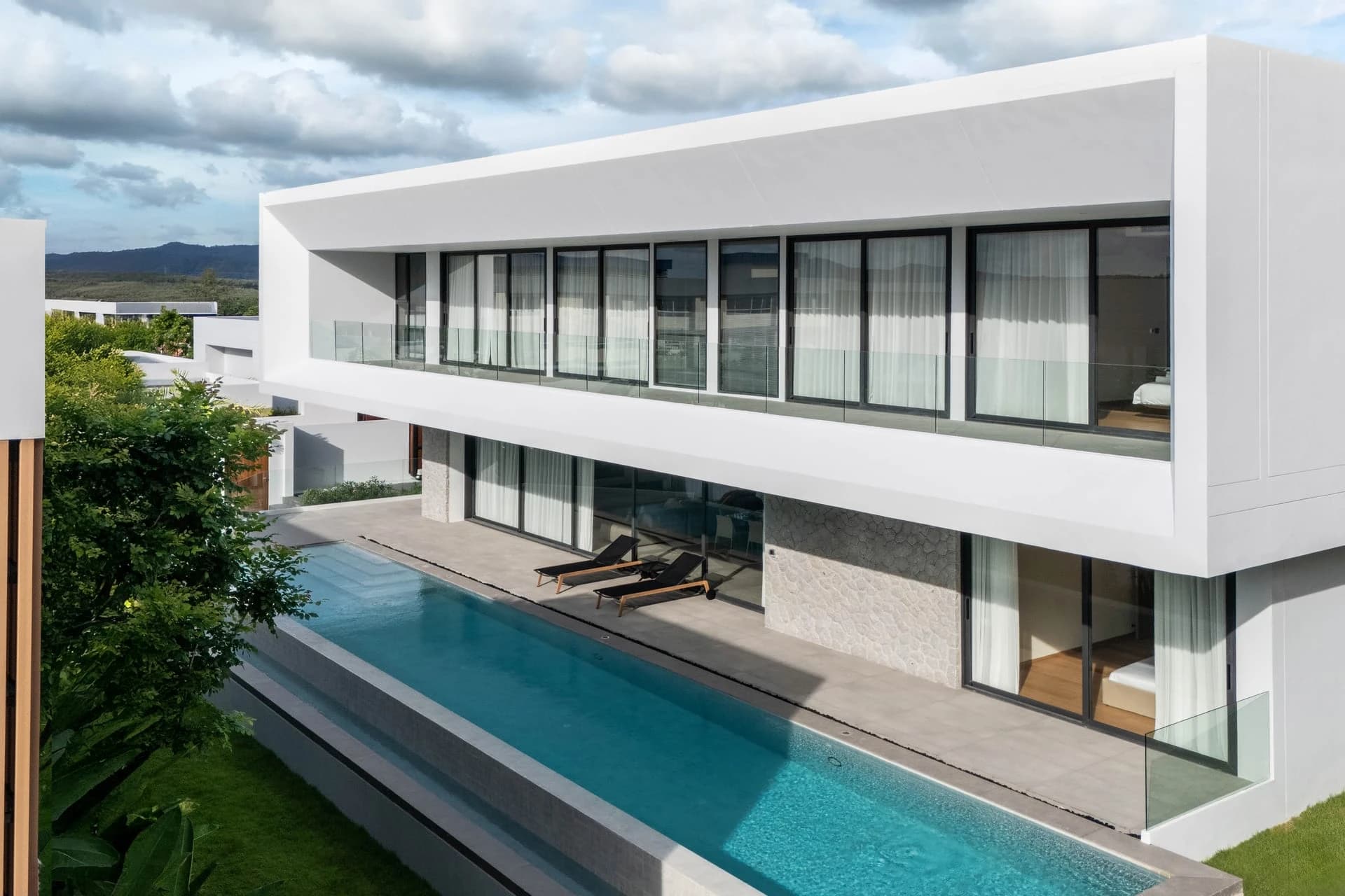Villa Typ A: der weiße Obergeschoss-Kubus mit raumhoher Verglasung über einem langen blauen Schwimmbecken
